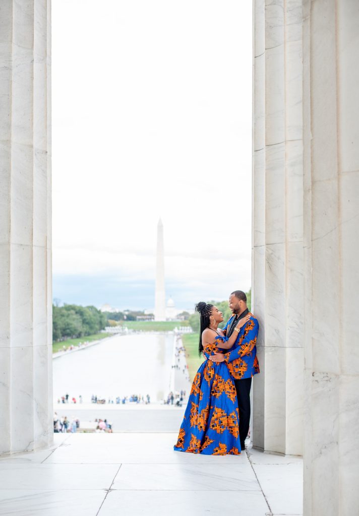 bride and groom wearing traditional Igbo attire lean against pillar at Lincoln Memorial with Washington Monument behind them