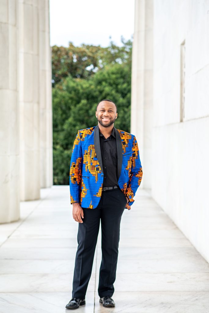 groom in blue and orange jacket poses in Lincoln Memorial