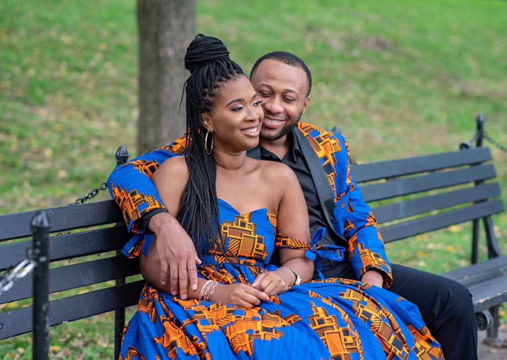 engaged couple in blue and orange traditional African attire poses on bench in DC