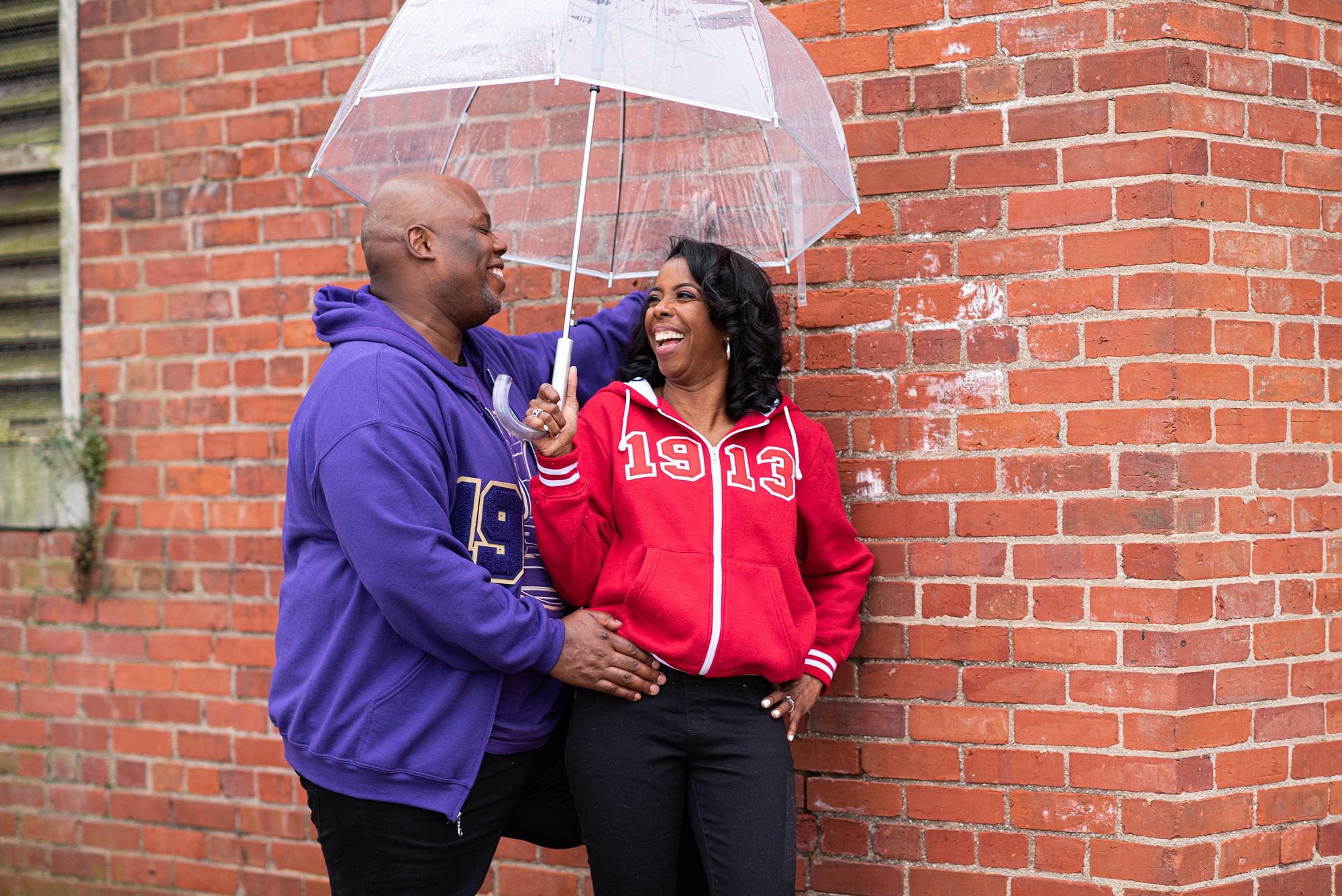 Maryland couple laughs under umbrella during engagement photos in Fort Washington Park
