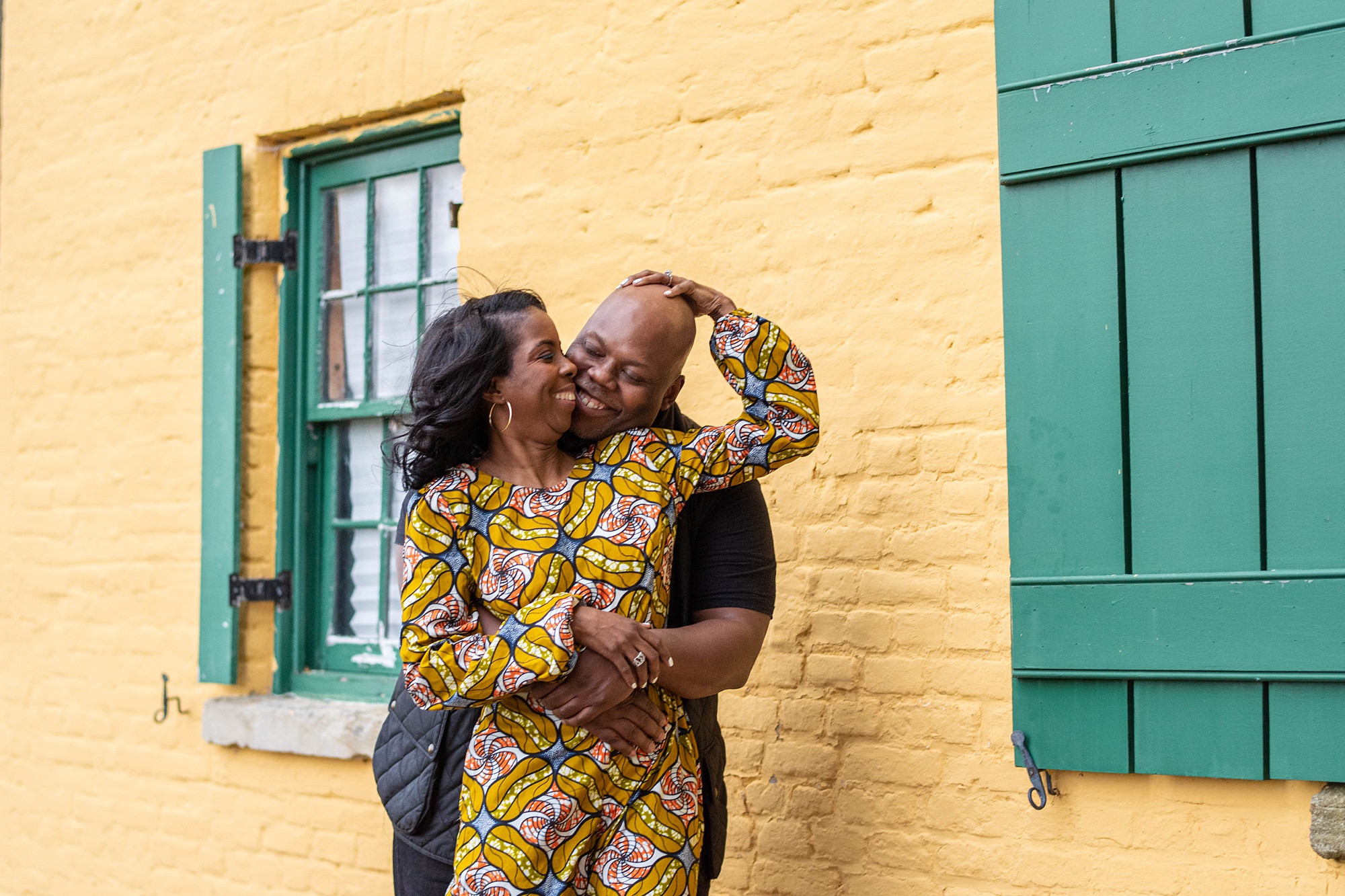 engaged couple poses by yellow wall in Maryland 