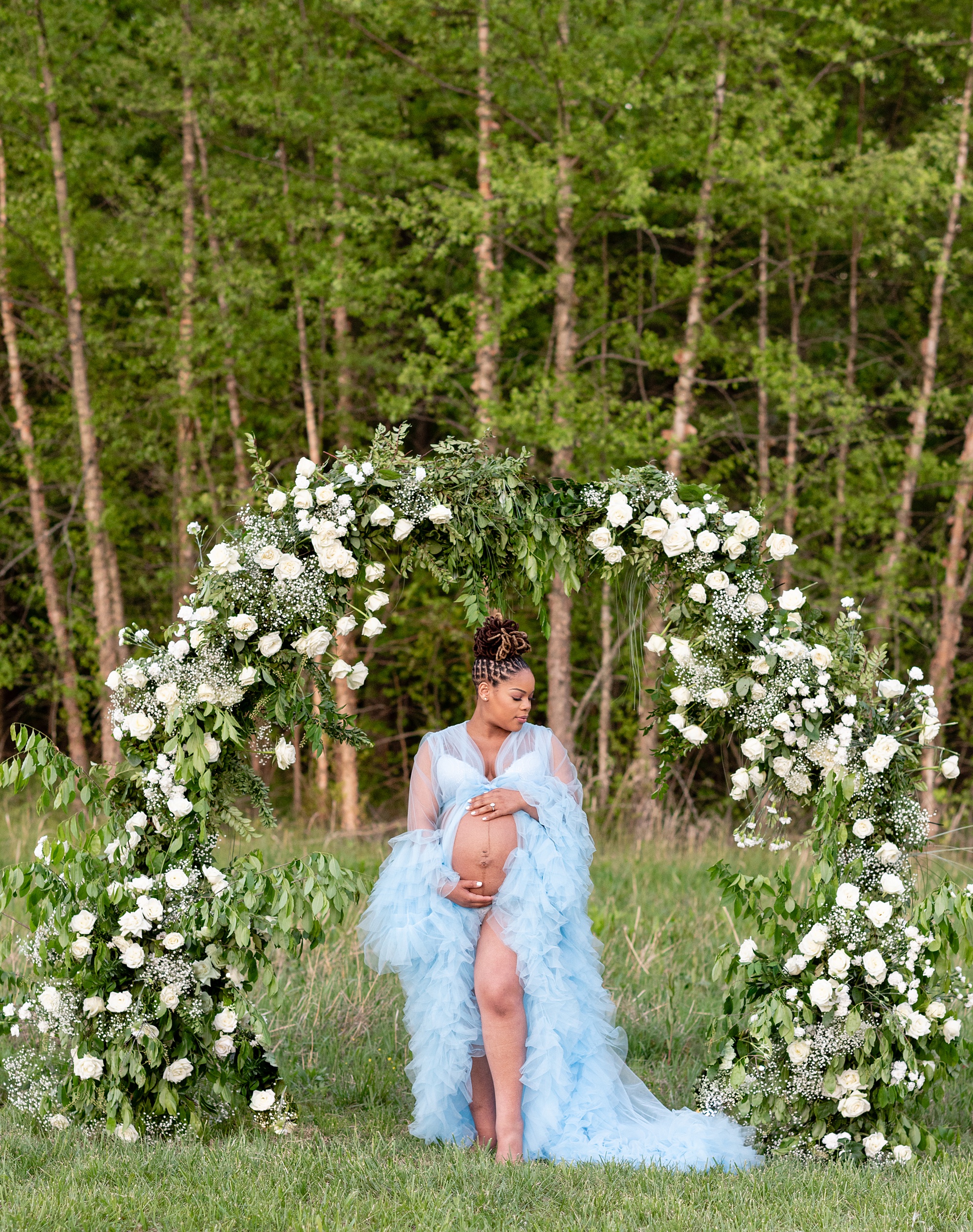 mom in flowing blue gown holds belly under arbor photographed by Washington DC maternity photographer