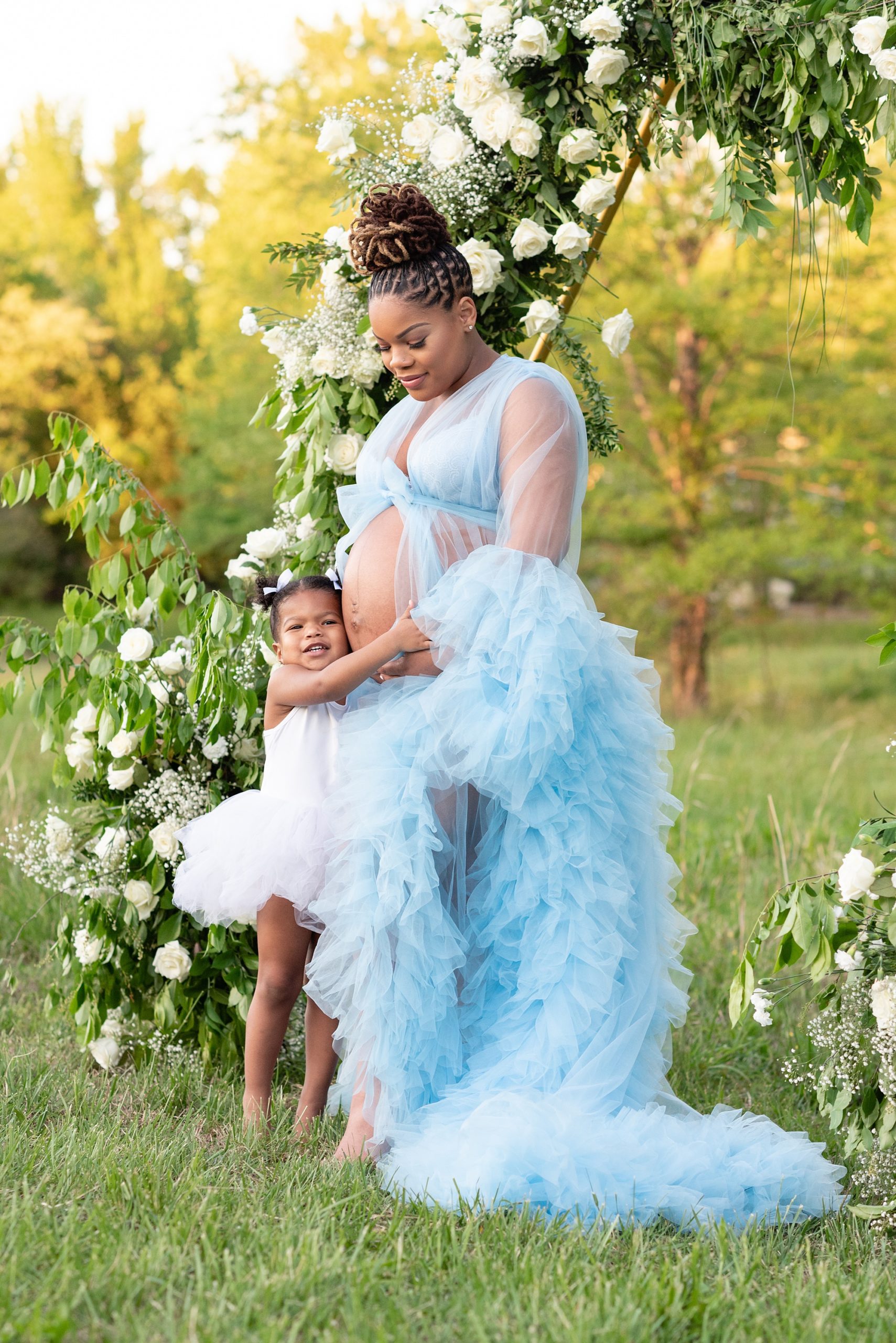 mom hugs toddler during maternity photos under floral arbor