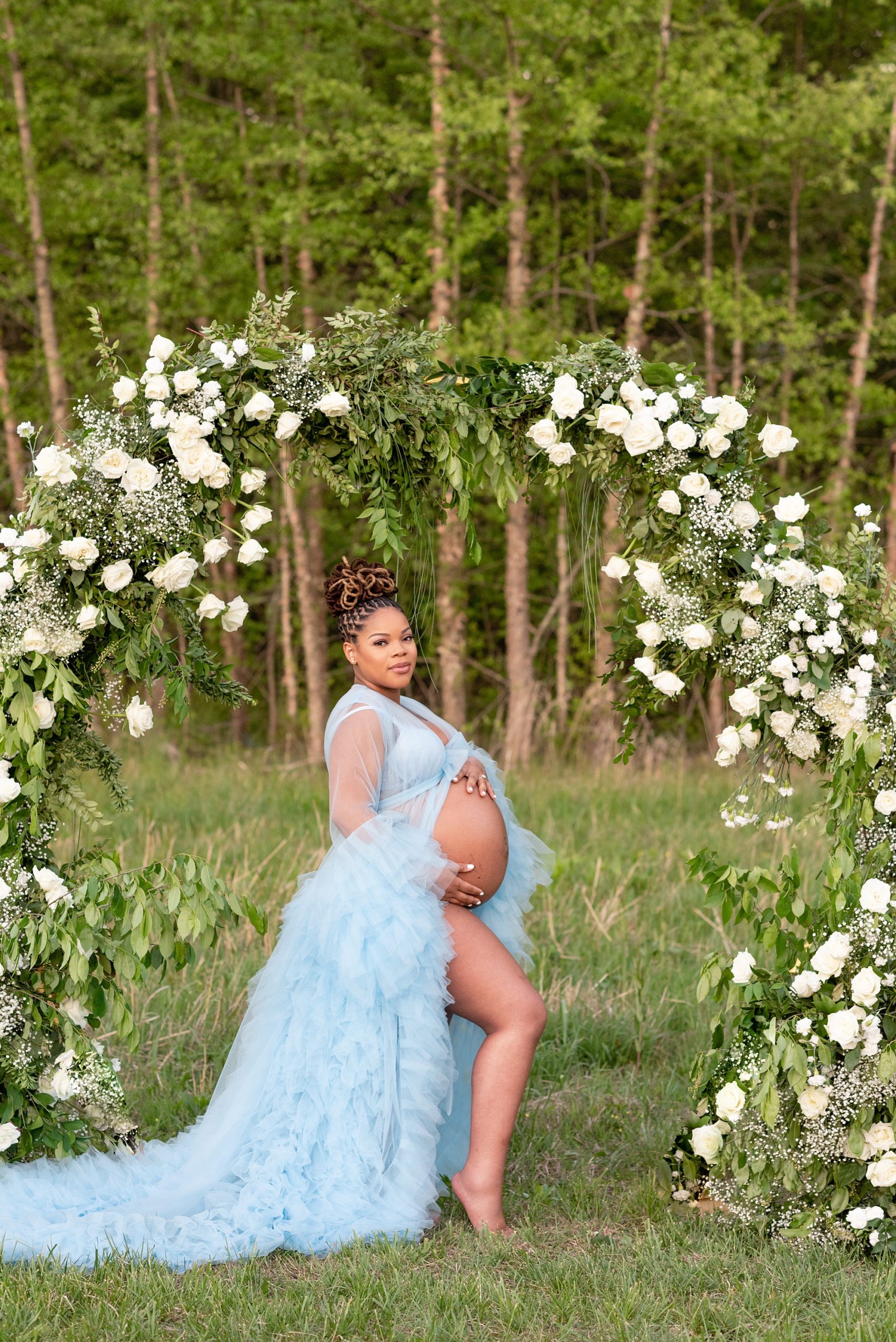 mom holds belly in blue gown during spring maternity photos 