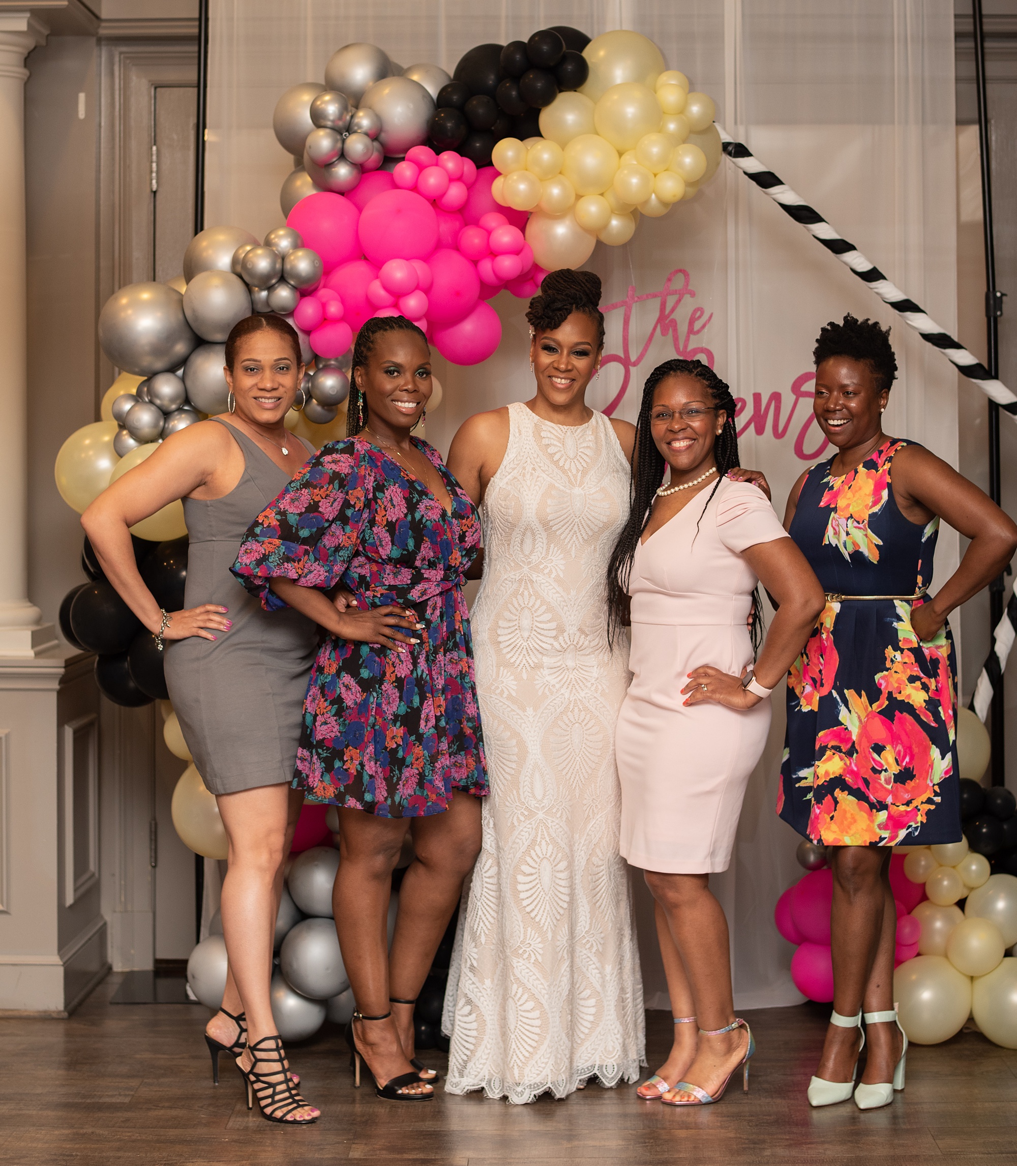 bride poses with friends under balloon arch 