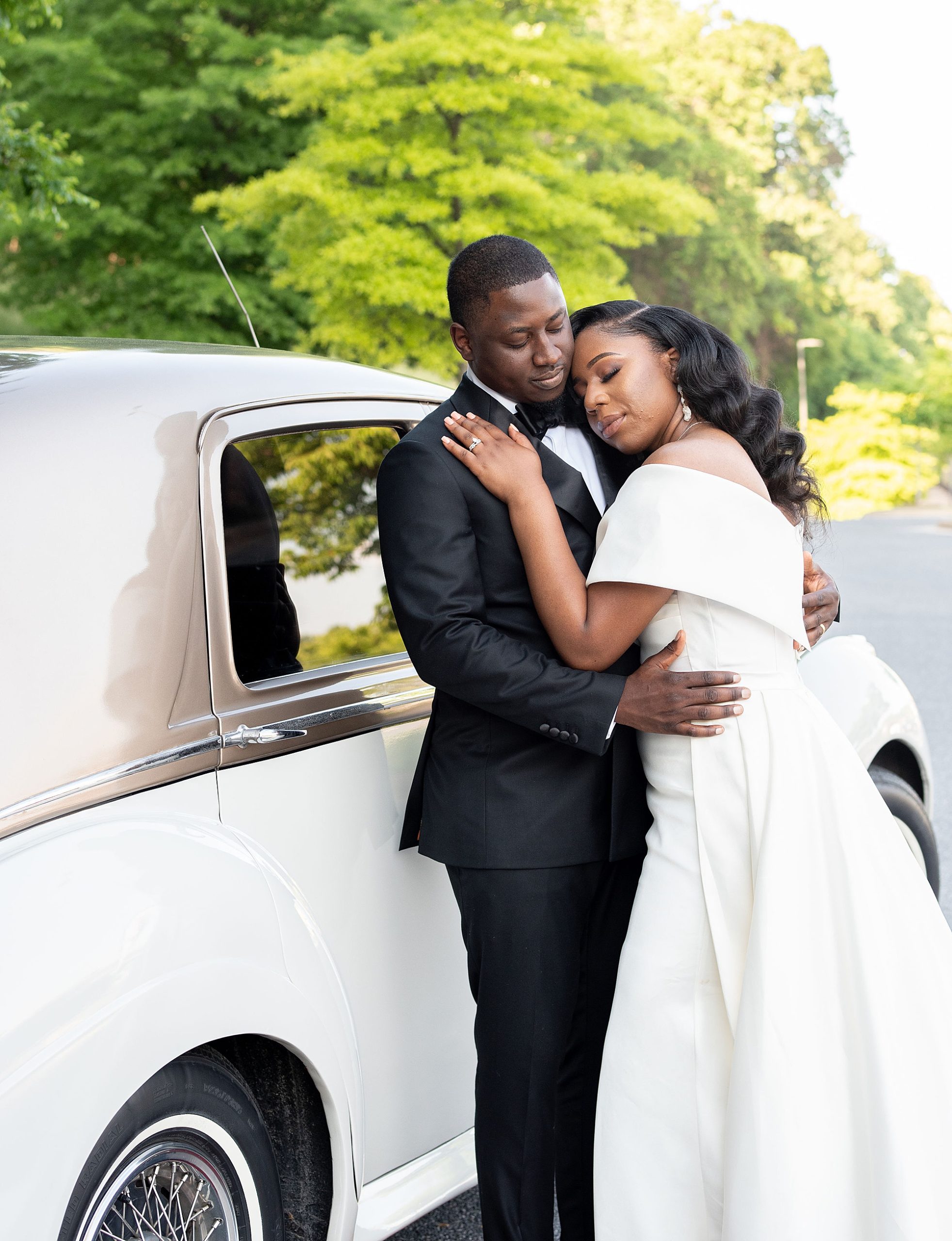 bride hugs groom leaning against classic car