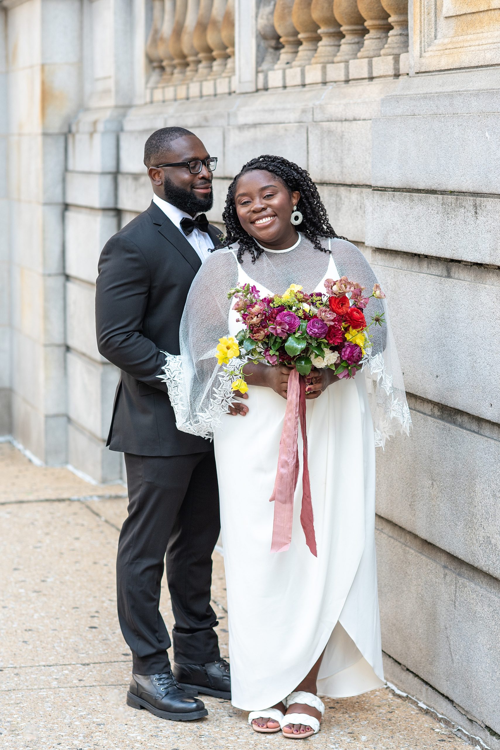 bride and groom pose alongside courthouse in Baltimore MD
