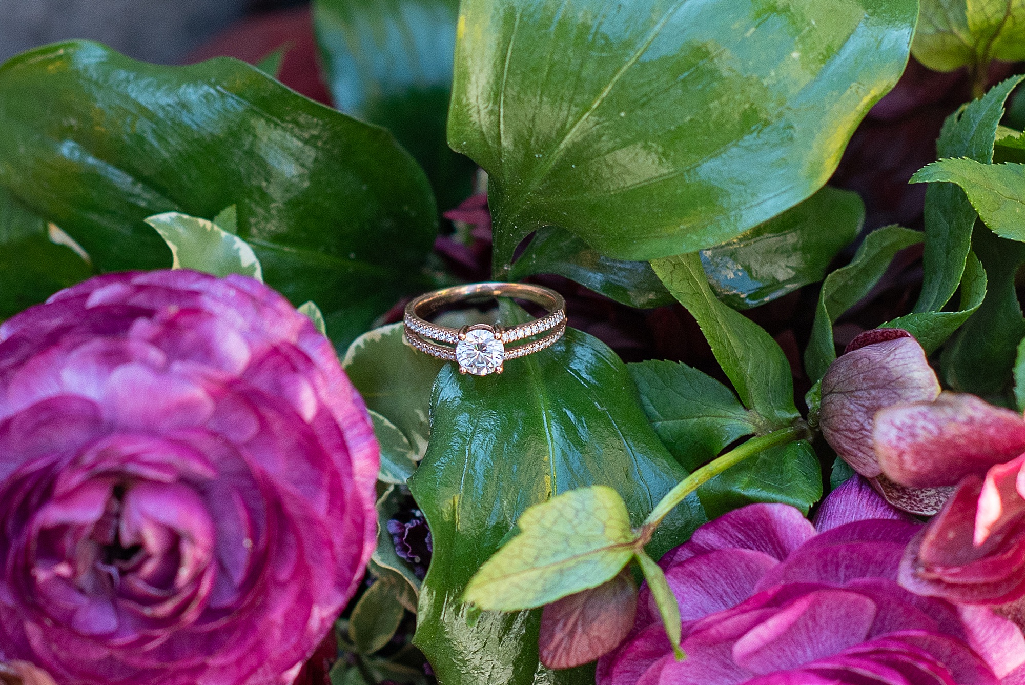 wedding rings rest on green leaf of bouquet 