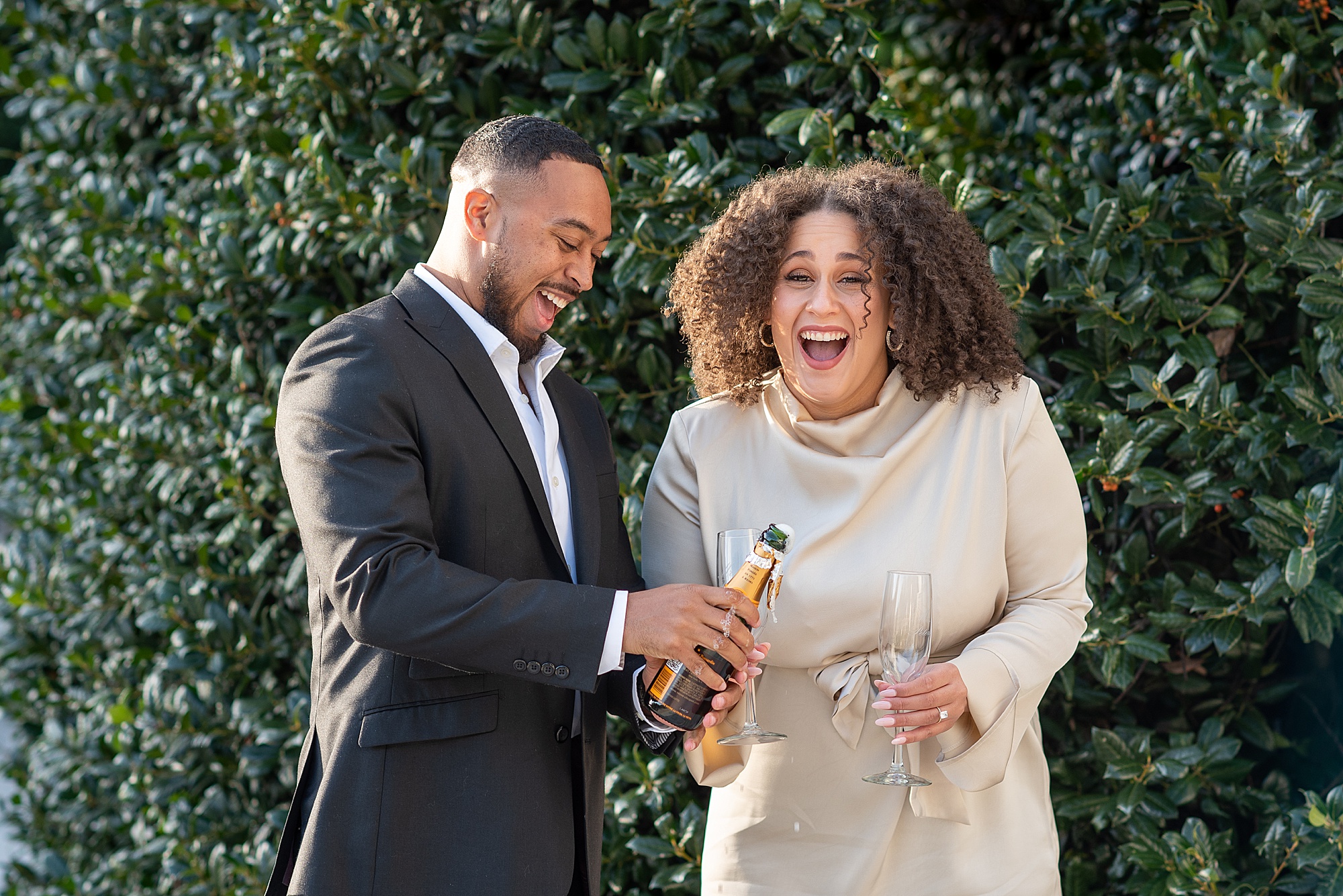 bride laughs while groom pops champagne during DC engagement photos