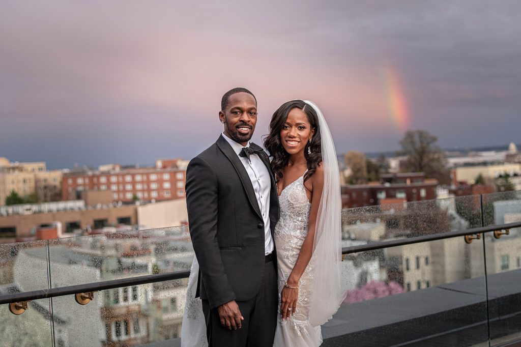 couple pose on the rooftop of LINE Hotel DC with rainbow in background